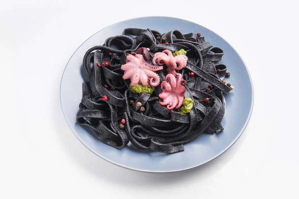 Mürekkepbalığı mürekkepli İtalyan siyah makarna ve beyaza izole edilmiş bir tabakta marine edilmiş ahtapot. Lezzetli Asya deniz ürünleri. - Fotoğraf, Görsel