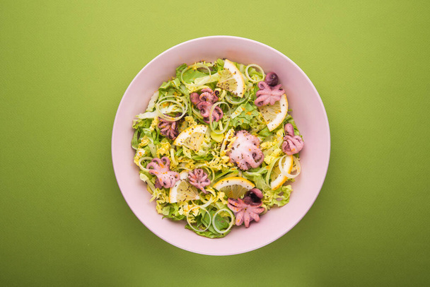 Čerstvý salát s chobotnicí, salátem a citrónem na zeleném pozadí. Jídlo z mořských plodů. Horní pohled - Fotografie, Obrázek