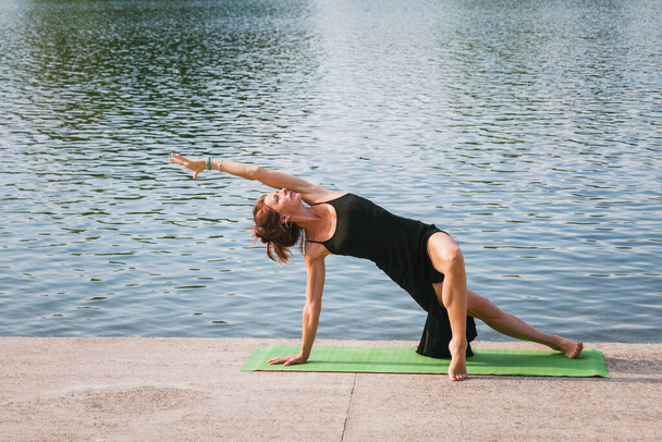 vrouw oefenen yoga zomer ochtend door het meer - Foto, afbeelding