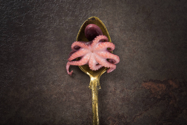 Маленький маринованный осьминог на золотой ложке, винтажный стол. Фон морепродуктов
 - Фото, изображение
