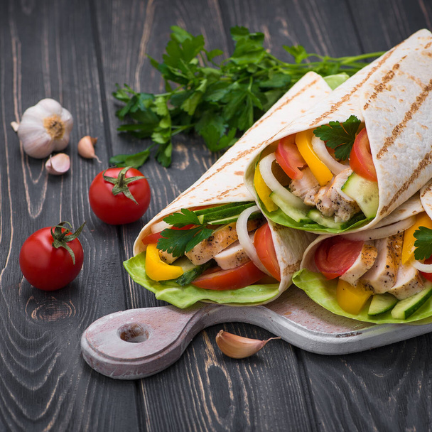 Tortilla wraps with grilled chicken and fresh vegetables on a wooden board. Mexican fast food background. - Photo, Image