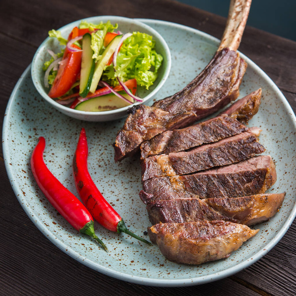 Tomahawk Rib Steak mit frischem Gemüse und Paprika auf einem Teller - Foto, Bild