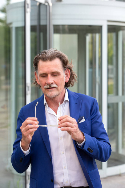 handsome businessman in his 50s standing outside holding his glasses - Foto, afbeelding