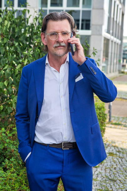 portrait of businessman in his 50s standing outside and talking on the phone - Valokuva, kuva