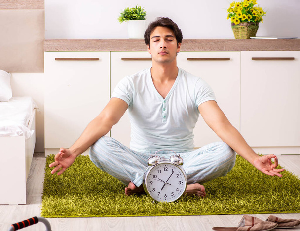 Giovane che fa yoga in camera da letto nel concetto di gestione del tempo - Foto, immagini
