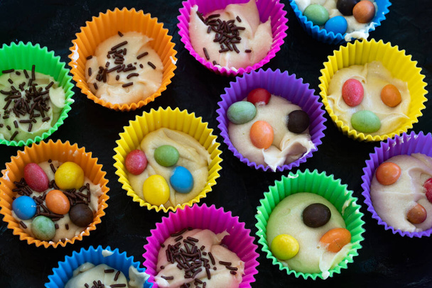 Домашні кекси в різнокольорових силіконових формах і з кольоровими шоколадними цукерками всередині на випічці. Смачна випічка, приготована вдома
. - Фото, зображення