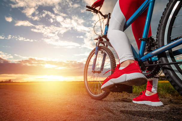 Beautiful girl in a red sports suit on a bicycle on a sunset background. The concept of a healthy lifestyle, sports training, cardio load. Copy space - Fotoğraf, Görsel