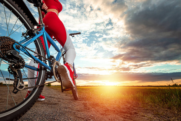 Sports training on a bicycle. Beautiful girl in a sports suit on a sunset background. The concept of a healthy lifestyle, cardio training, physical activity. Copy space - Fotó, kép