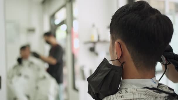 view from behind inside men Barbershop, Asian man with black mask get hair cut. mirror reflection, sharp edge sideburns, gentlemen barber during Corona Covid-19 re-open business after Pandemic - Footage, Video