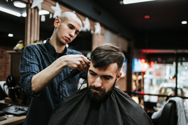 Good looking young adult man getting a hair and beard styling and dressing treatment by professional hairstylist. - Photo, Image