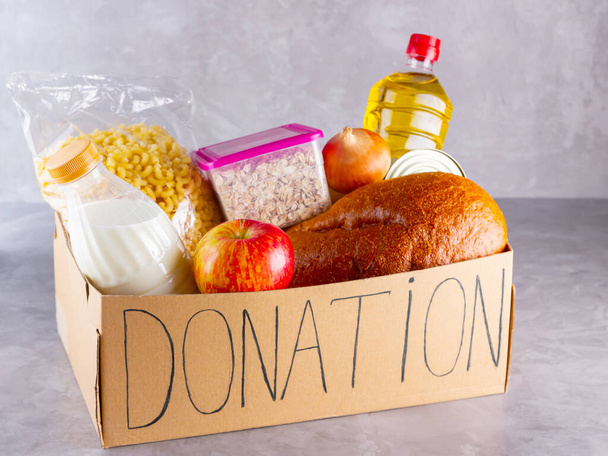 Donation box with food. Open cardboard box with oil, milk, canned food, pasta and bread. Grocery set on gray background. Donation concept - Valokuva, kuva