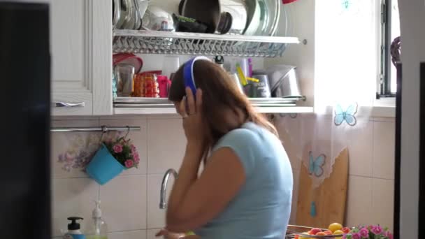 νεαρή γυναίκα πλένει τα πιάτα ακούγοντας μουσική με ακουστικά - Πλάνα, βίντεο