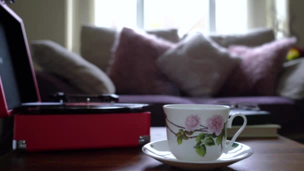 Miękkie skupienie wirującej płyty winylowej odtwarzacza z zamazaną filiżanką gorącej kawy lub filiżanką herbaty z parą w filtrze retro, Przytulne i relaksujące sceny popołudniowej herbaty w pokoju konserwatorium - Materiał filmowy, wideo