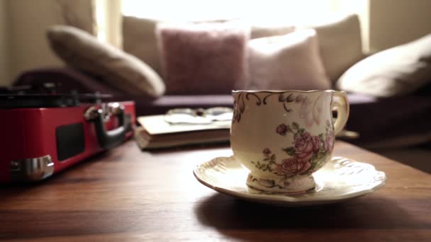 Weicher Fokus des sich drehenden Plattenspielers mit verschwommener Tasse heißem Kaffee oder Tasse Tee mit Dampf im Retro-Filter, gemütliche und entspannende Szene des Nachmittagstees im Wintergarten - Filmmaterial, Video