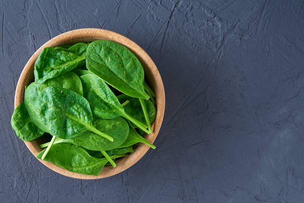 Fresh spinach leaves in wooden bowl on a dark background. Organic food - Foto, Imagen