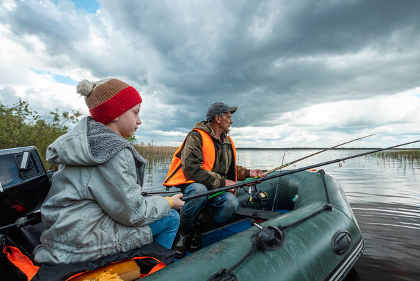 Il nipote e il nonno insieme pescano da una barca sul lago. Il concetto di famiglia, vacanze estive, generazione. Copia spazio - Foto, immagini