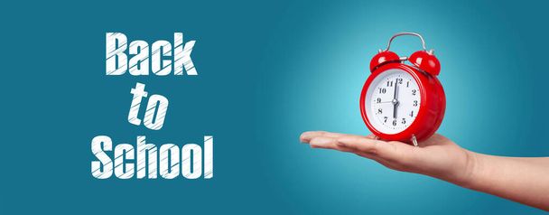 κόκκινο ρολόι με συναγερμό στο χέρι πάνω από το μπλε φόντο, πανοραμική εικόνα με επιγραφή πίσω στο σχολείο - Φωτογραφία, εικόνα