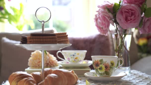 Traditionelle englische Teezeit, Nachmittagsteezeremonie mit Cuppa Tea, Croissants, Crackern und Keksen auf hohem Teeständer in rosa Pastell. Gemütliche Nachmittagsparty im Wintergarten - Filmmaterial, Video