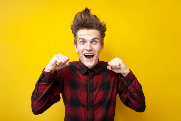 guy winner with a funny hairstyle screams yes on a yellow isolated background, hipsters rejoice in victory and celebrate success - Foto, immagini