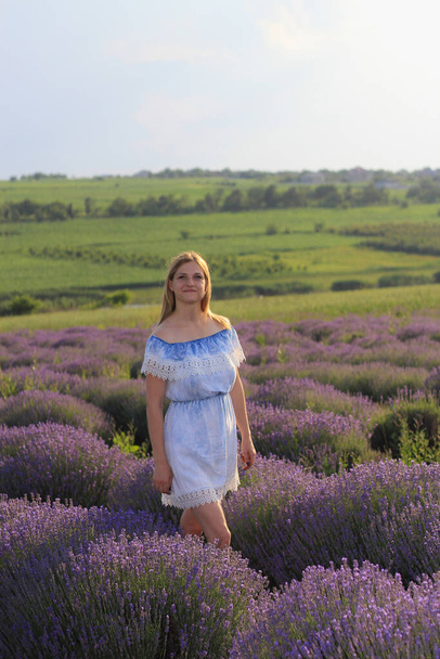 Lifestyle photo shoot in nature. A girl or young woman enjoys a walk through the fresh air and the scent of a lavender field in the sunset. Selective focus. - Fotó, kép