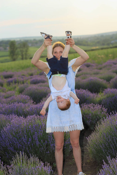 Lifestyle photo shoot of a real family in nature. Mom and son enjoy a stroll through the fresh air and scent on a lavender field in the rays of the setting sun. Selective focus. - Foto, Bild