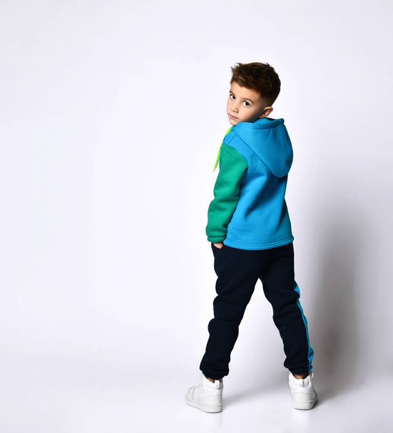 Little boy in colorful sport suit, sneakers. He looking back, posing standing back to camera, isolated on white studio - Fotó, kép