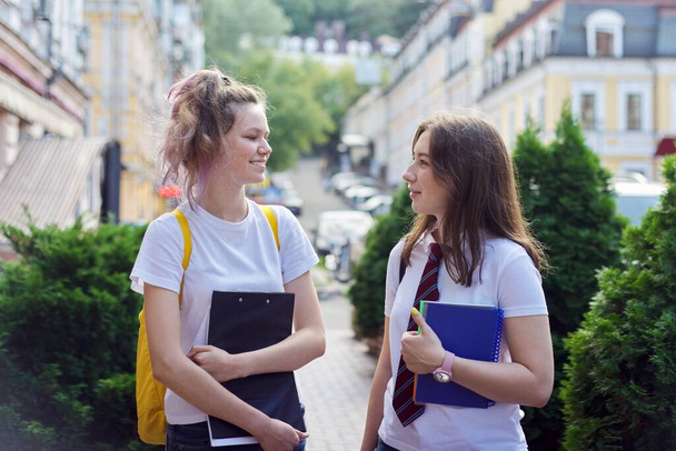 Two girl students talking on a city street, teenagers with backpacks - Valokuva, kuva