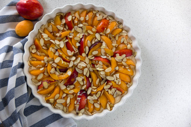 tarte maison aux abricots, tranches d'abricots mûrs et nectarines à la surface de la pâte dans un plat de cuisson blanc - Photo, image