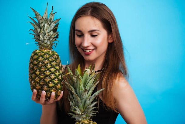 portrait of a girl on a blue background holding pineapples - Foto, Imagem