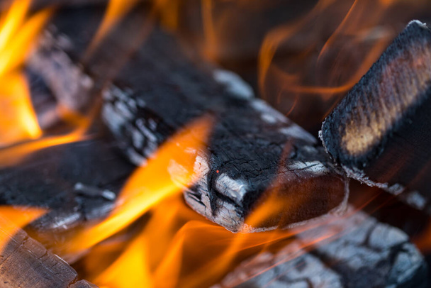 Flame incinerates firewood and transforms it ashes, close up, shallow depth of field. Blaze in a large stove. Nature texture of fire. The flame of fire burns in the brazier, smoldering firewoods. - 写真・画像