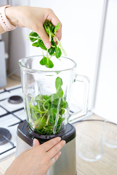 Girl hands prepare a green smoothie, puts fresh spinach leaves in a blender. Healthy eating concept. Vegetarianism, vegan food, fitness food, detox, youth preservation. - Photo, Image