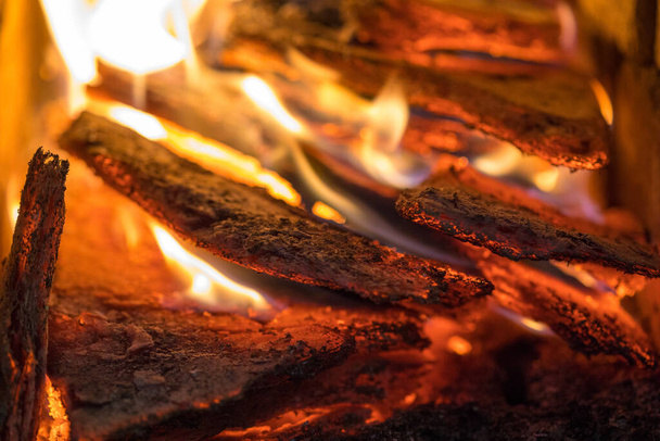 Flame incinerates firewood and transforms it ashes, close up, shallow depth of field. Blaze in a large stove. Nature texture of fire. The flame of fire burns in the brazier, smoldering firewoods. - Photo, Image