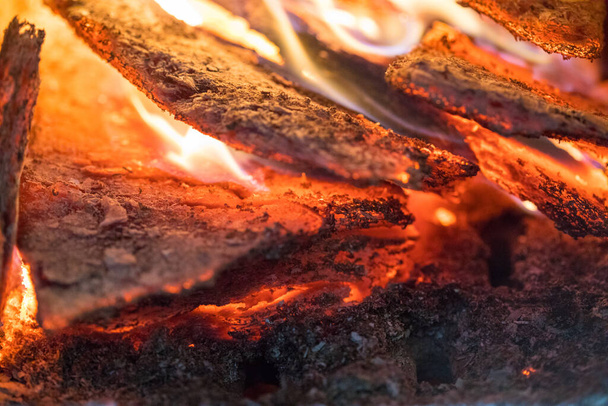 Plamen spaluje dřevo na podpal a přeměňuje ho na popel, zblízka, mělkou hloubku pole. Plamen ve velkém sporáku. Přírodní textura ohně. Plamen ohně hoří v pánvi, doutnající dřevo. - Fotografie, Obrázek