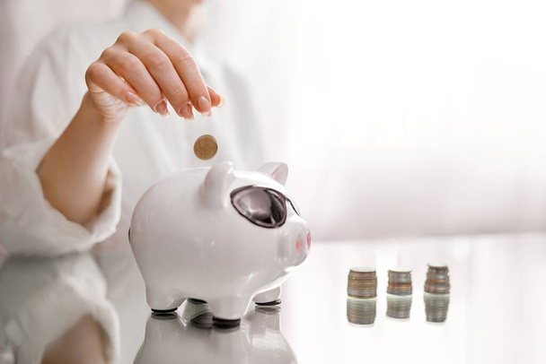 Woman throws coins in pig piggy bank from stacks - Photo, Image