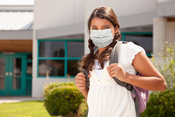 Ισπανίδα μαθήτρια με μάσκα προσώπου και σακίδιο στο σχολείο. - Φωτογραφία, εικόνα