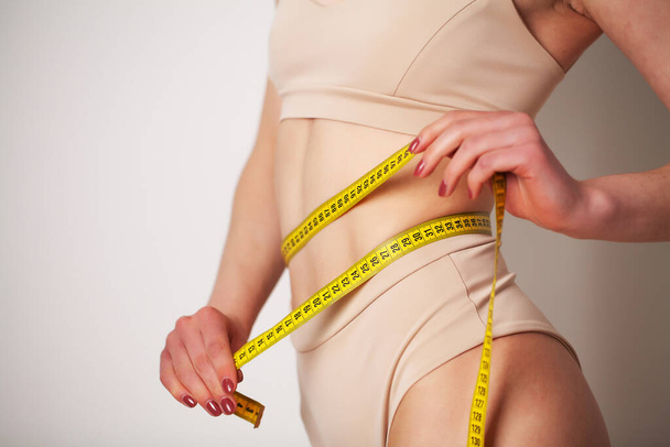 Spor vücutlu bir kadın belinin ölçüsünü alır. - Fotoğraf, Görsel