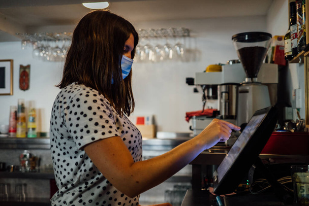 Kaukaska właścicielka kawiarni, bizneswoman przyjmująca zamówienia od klienta przy kasie, używając tabletu cyfrowego. Nosi maskę na twarzy. działalność otwarta po kwarantannie - Zdjęcie, obraz