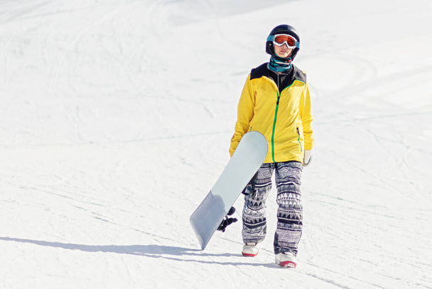 Jeune femme snowboarder marchant sur la piste de ski tenant son snowboard, elle regarde la caméra, copier l'espace. - Photo, image