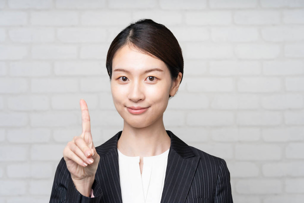 Porträt einer jungen asiatischen Geschäftsfrau, die mit erhobenem Zeigefinger posiert - Foto, Bild