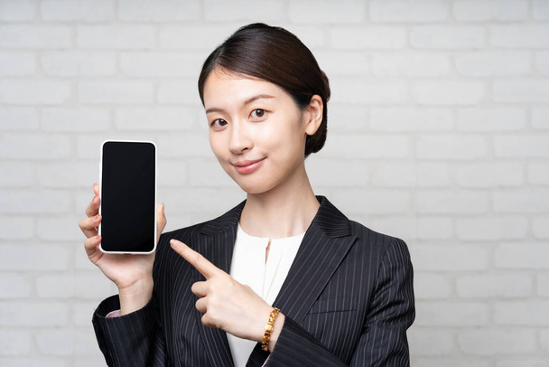 Азиатская молодая деловая женщина в костюме оператора экрана смартфона
 - Фото, изображение