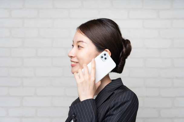 Азиатская молодая деловая женщина в костюме разговаривает со смартфоном рядом с ухом
 - Фото, изображение
