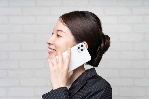 Asiatique jeune femme d'affaires dans un costume parler avec le smartphone près de l'oreille - Photo, image