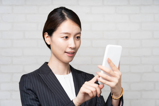 Asiatique jeune femme d'affaires en costume opérant écran smartphone - Photo, image