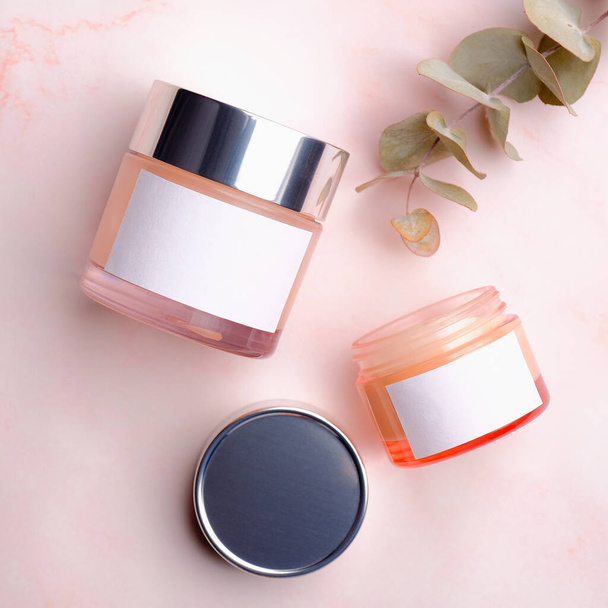 Skincare product packaging mockup. Jars of cosmetic cream with white labels and eucalyptus leaf on pink background. Flat lay, top view. - Foto, Imagen