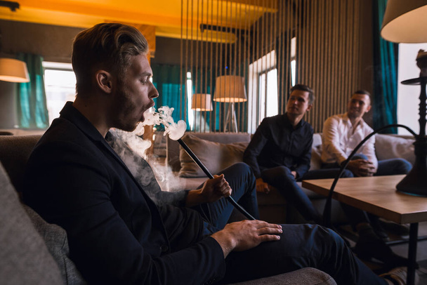 Men relax and smoke hookah in a stylish loft cafe with a modern design - Zdjęcie, obraz