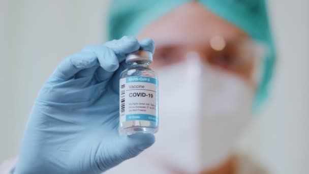 Doctor in protective hazmat suit shows bottle with Covid-19 vaccine in liquid - Felvétel, videó