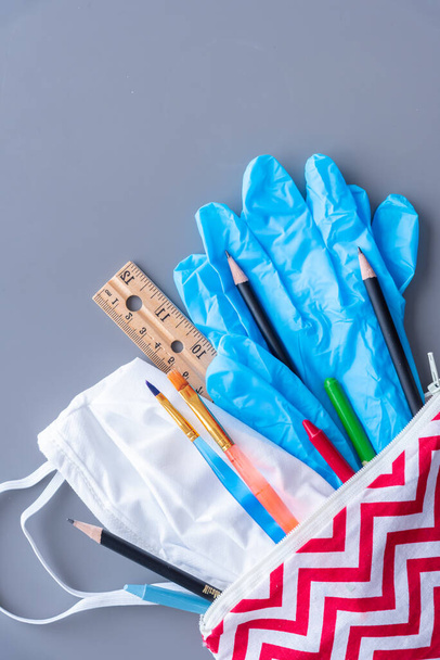 Child's pencil case filled with school supplies, surgical mask and gloves. Flat lay on grey background - Foto, immagini