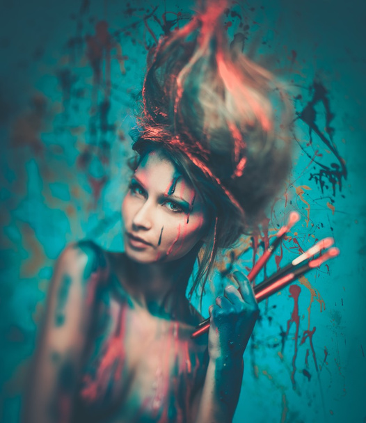 Young woman muse with creative body art and hairdo holding paint brushes - Photo, Image