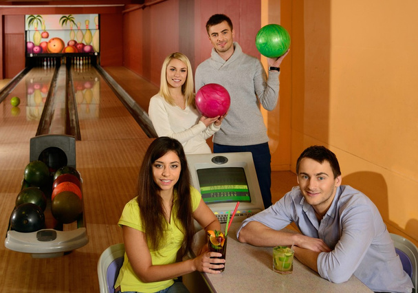 vier jonge mensen in bowlingclub met ballen en dranken - Foto, afbeelding
