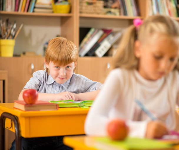 Little redhead schoolboy behind school desk during lesson - Fotoğraf, Görsel